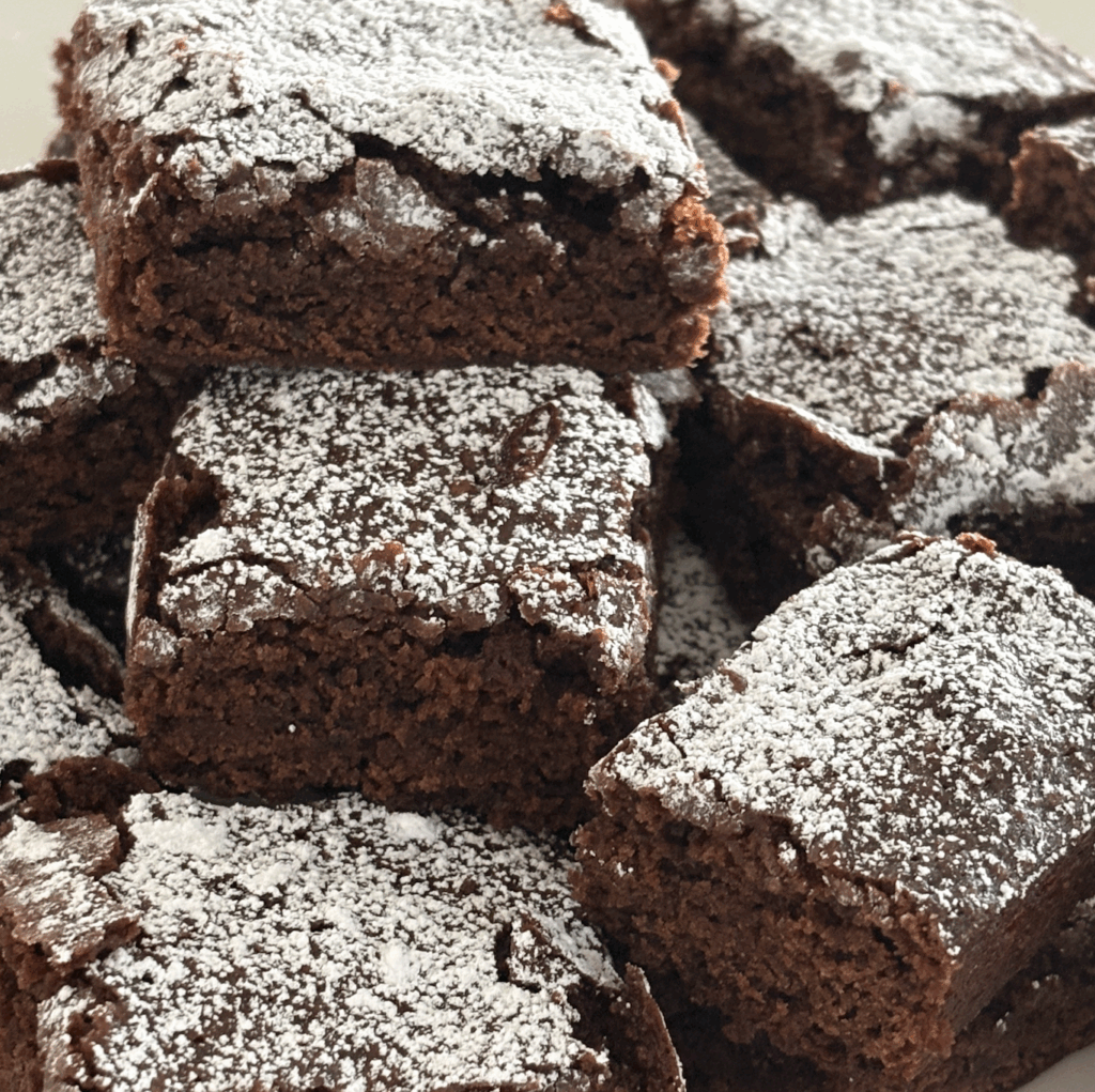Close-up of soft, rich egg-free and dairy-free brownies dusted with powdered sugar, showing their moist, cakey texture.