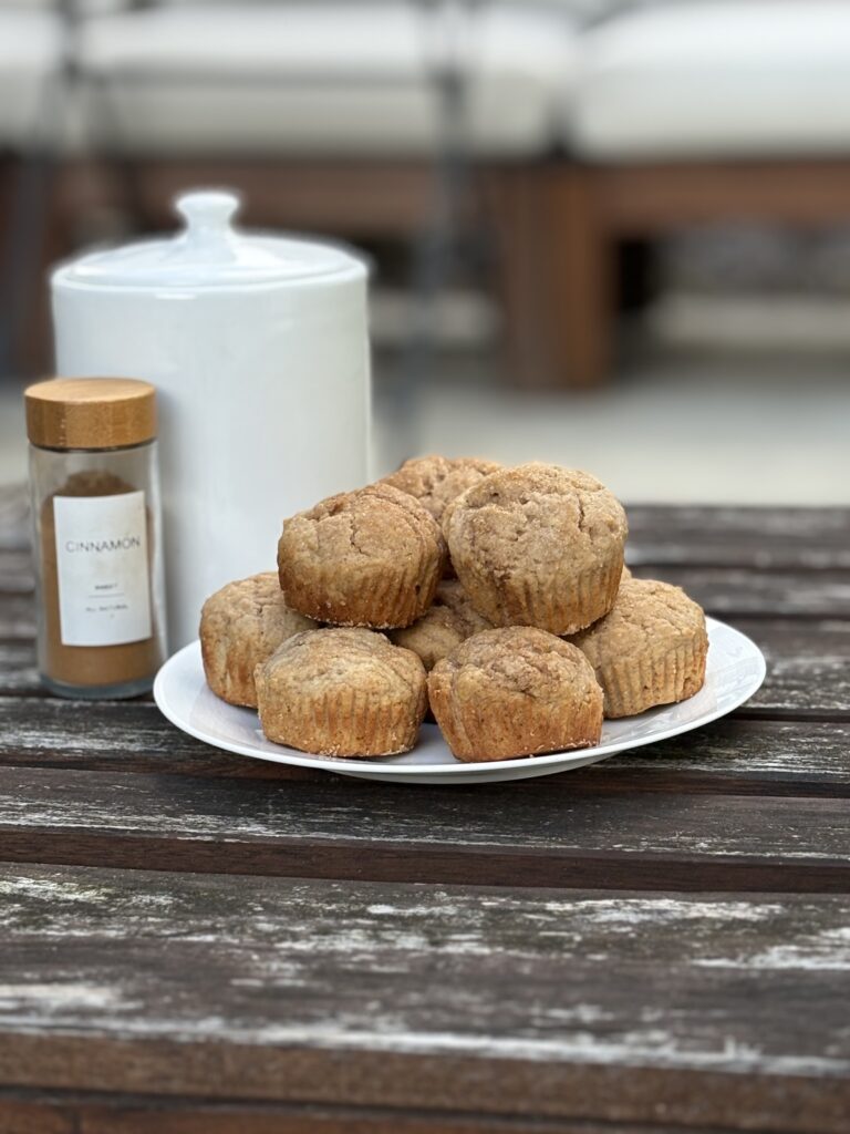 A stack of soft, egg-free, nut-free cinnamon muffins on a white plate, sitting on a rustic wooden table with a jar of cinnamon nearby.
