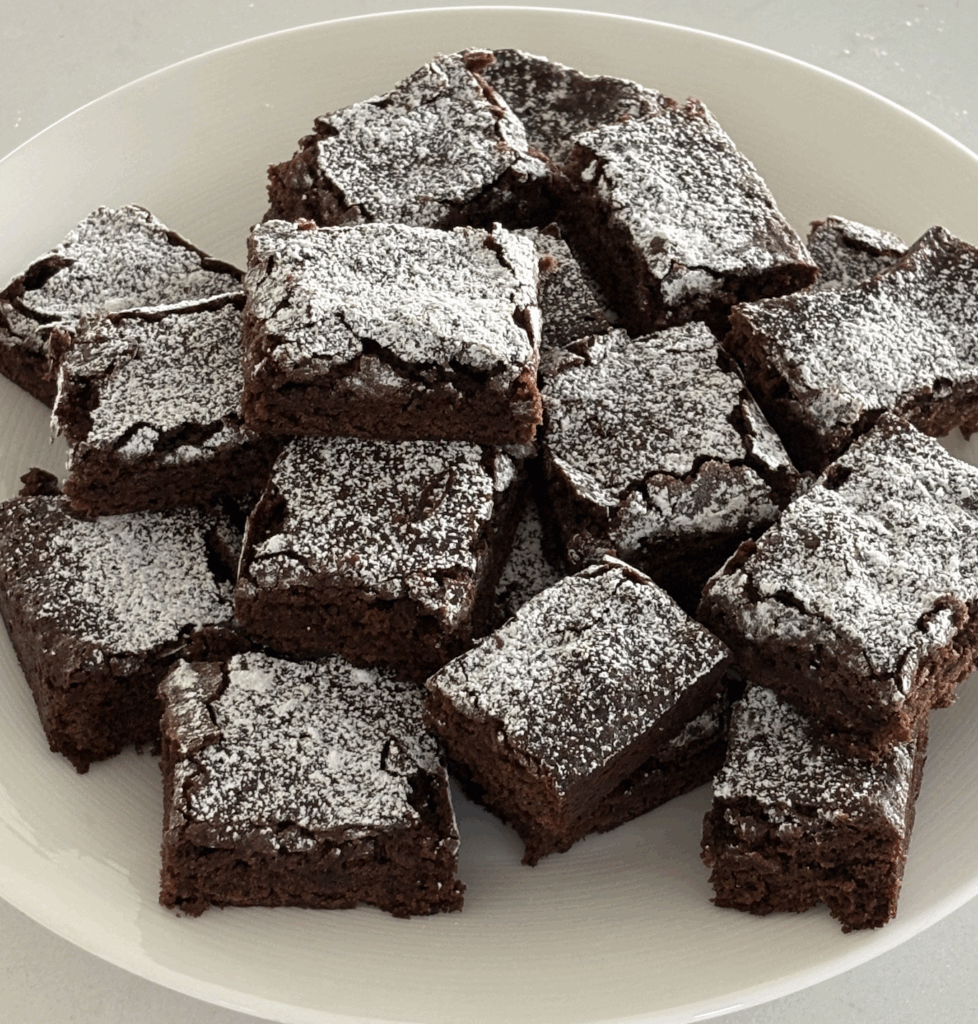 Plate of soft, rich egg-free and dairy-free brownies dusted with powdered sugar on a white plate.
