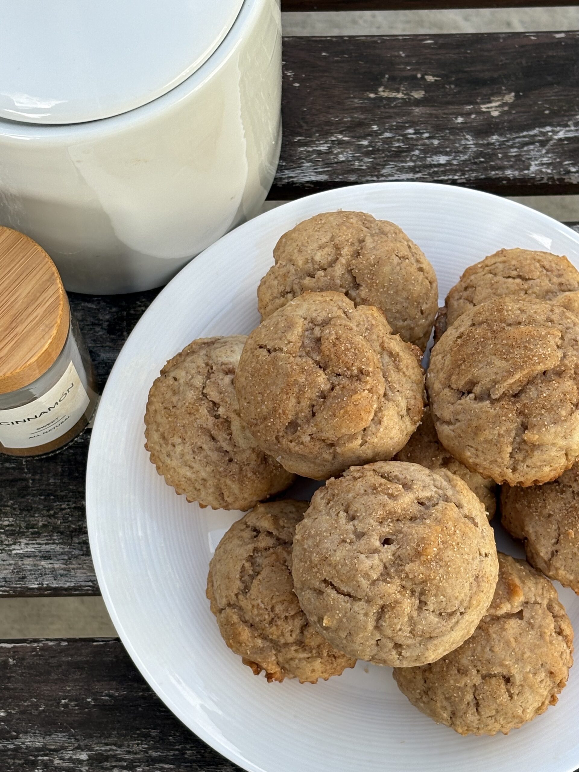 Overhead view of golden brown cinnamon muffins topped with cinnamon sugar on a white plate, next to a cinnamon spice jar.