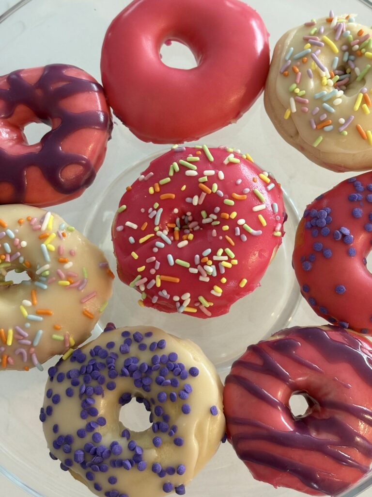 Close-up of air fryer donuts with pink glaze, purple drizzle, and sprinkles.